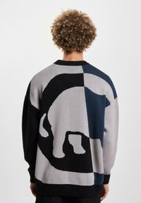 Knit sweater featuring a geometric pattern in navy, gray, and black, with a prominent polar bear silhouette on the back and ribbed cuffs.