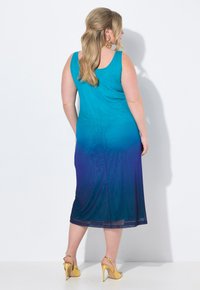 Abito senza maniche in ombre teal a viola con un design fluido, texture morbida, e orlo leggermente trasparente, abbinato a sandali con tacco dorato.
