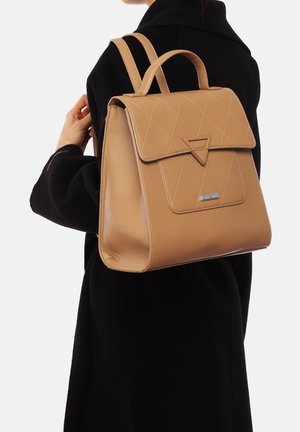 Mochila de cuero marrón claro con un diseño acolchado, acento triangular en la solapa y doble correas para los hombros. Textura suave, forma elegante y hardware minimalista.