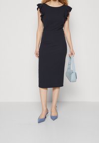 Mekko, jossa on tummansiniharsot, röyhelöhihat, istuva muotoilu ja sileä pinta. Yhdistetty vaaleansiniseen käsilaukkuun ja samansävyisiin kärjettyihin korkokenkiin.