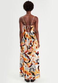 Abito lungo con spalline sottili regolabili, fantasia astratta colorata che presenta arancione, nero e bianco, e un taglio sulla schiena con un dettaglio a fiocco.