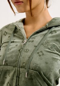 Green velour zip-up hoodie featuring subtle all-over print of crowns, diamonds, and apples. Includes drawstring hood and silver hardware accents.