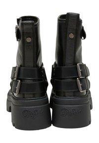 Botas de tobillo de cuero negro con una suela gruesa, que presentan dos correas ajustables, hebillas metálicas y un logo prominente en la parte trasera.