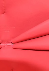 Heldere koraal leren met een gladde textuur, voorzien van een zichtbare rits en gestikte randen. Het ontwerp omvat gevouwen secties.