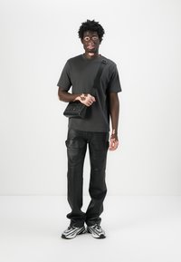 T-shirt noir, pantalon en cuir noir de style cargo et un petit sac noir avec une bandoulière. Associé à des baskets blanches et noires.