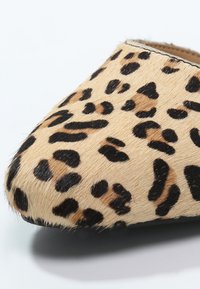 Chaussure plate à imprimé léopard avec un bout pointu, fabriquée en matériau doux et texturé, présentant un fond beige et des taches noir-brun.
