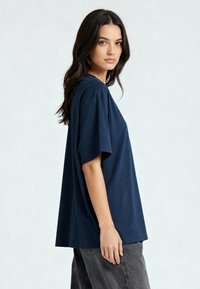 Tamsiai mėlynas per didelis marškinėliai, pagaminti iš minkštos medžiagos. Trumpomis rankovėmis, laisvas kirpimas, apvaliu kaklu, derinami su pilkais džinsais.