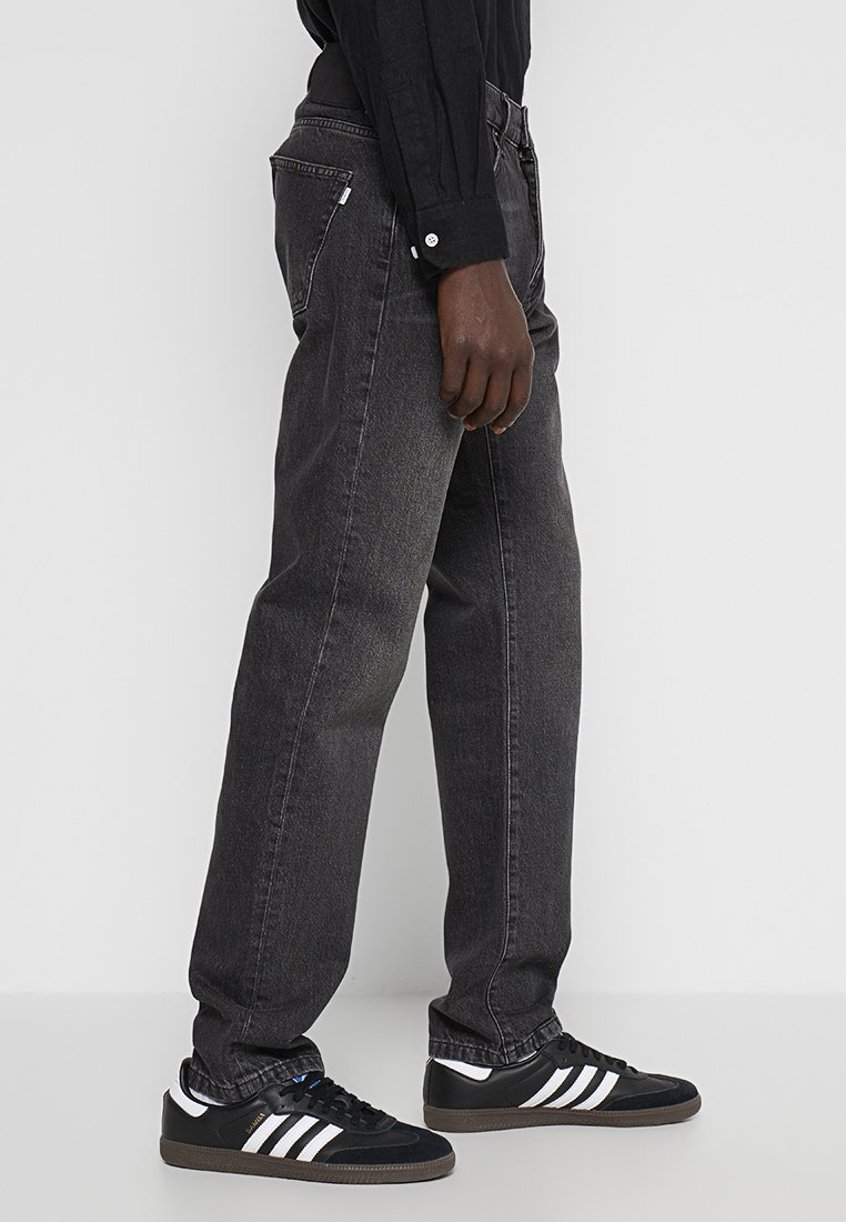 Zwarte spijkerbroek met een rechte pasvorm, met achterzakken en een subtiele vervaagde textuur, gecombineerd met zwarte sneakers met witte strepen.