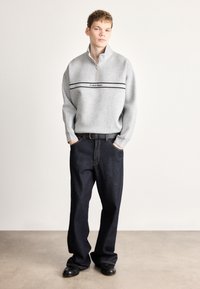 Γκρι φούτερ με φερμουάρ, μαύρη ρίγα και λογότυπο, σε συνδυασμό με σκούρο μπλε τζιν άνετης, πλατιάς εφαρμογής και μαύρα παπούτσια. Ομαλό ύφασμα και casual εφαρμογή.