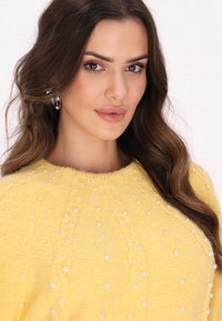 Pulover tricotat galben cu embellishments din perle și decolteu rotund. Textură moale și model complicat cu fire împletite vizibile pe întreaga suprafață.