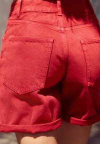 Röda denimshorts med hög midja, uppliggda fållar och två bakfickor med fyrkantiga klaffar. Materialet har en slät textur.