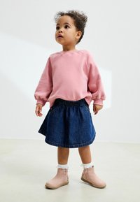 Sudadera de algodón rosa con mangas abullonadas, falda de mezclilla azul y botas rosas hasta el tobillo con puños blancos con volantes y acentos florales.
