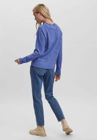 Blue knitted sweater with a textured pattern, crew neckline, and ribbed cuffs, paired with denim jeans and beige boots.