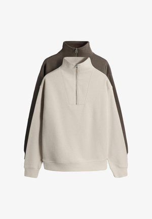 Két negyed cipzáros, hosszú ujjú pulóver álló gallérral, egyik elöl bézs, másik hátul sötétbarna, fehér háttér előtt bemutatva.