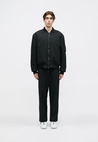 Melnā bomber jaka ar rāvējslēdzēju priekšpusē un ribotām piedurknēm, apvienota ar vaļīgiem melniem biksēm un baltām sporta apaviem. Minimalistisks dizains.