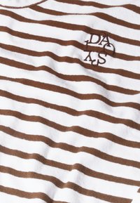 Camiseta de algodón a rayas en blanco y marrón, con cuello redondo y detalle de logo bordado. Tejido texturizado con acabado suave.
