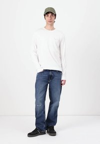 Wit overhemd met lange mouwen, blauwe spijkerbroek, zwarte sneakers en groene pet. Eenvoudig ontwerp, casual pasvorm, gladde textuur, minimale details.
