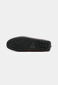 Semelle en caoutchouc noir avec un motif de grip texturé, partie supérieure lisse en marron et design de talon arrondi, avec un logo sur le côté.