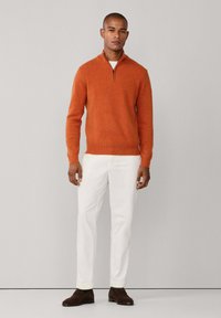 Maglione arancione con zip, realizzato in morbido tessuto a maglia, abbinato a pantaloni bianchi e scarpe marrone scuro. Design semplice e moderno.