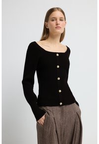 Svart ribbstickad långärmad tröja med fyrkantig urringning och guldfärgade knappar framtill. Matchas med bruna texturerade vida byxor.