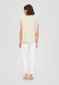 Jasnozielona bluzka w białe paski bez rękawów w połączeniu z białymi lnianymi spodniami. Modelka nosi sandały na platformie w neutralnych odcieniach.