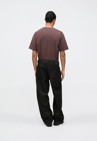 Jeans de ganga escura com um ajuste relaxado e bolsos traseiros visíveis, combinados com uma t-shirt de mangas curtas em tom roxo suave. Design simples, sem padrões.