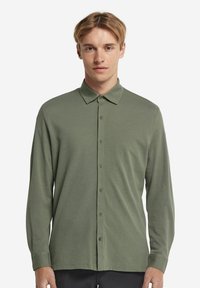 Långärmad skjorta med knappar i olivgrön, tillverkad av mjukt tyg. Har en klassisk krage och knappframställning.