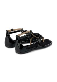 Sandali in pelle patent nera con suola piatta, cinturini alla caviglia e decorazioni floreali. Plantare testurizzato e finitura liscia.