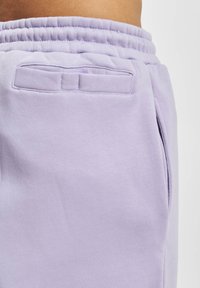 Lichtpaarse sweats met een zachte textuur, een elastische tailleband en een achterzak met een klein flapje. Zakken aan de zijkanten zijn zichtbaar.
