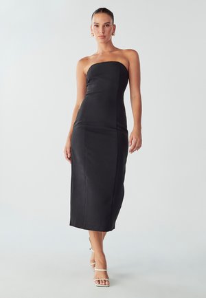 Black strapless midi dress, fitted design, smooth texture, with simple seam details. Model wears white strappy heels.