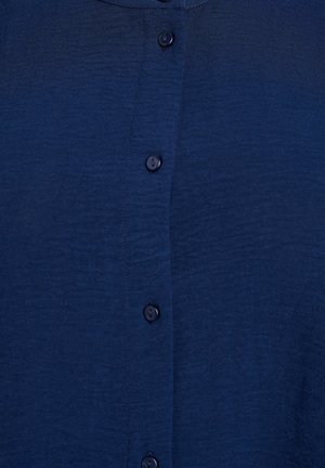 Námořnická modrá košile s knoflíky vyrobená z lehké látky, s texturovaným povrchem a šesti tmavými knoflíky na přední straně.
