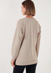Felpa beige chiaro con scollatura a girocollo e maniche lunghe. Presenta una vestibilità rilassata, polsini a coste e un orlo con spacchi laterali. Texture liscia.
