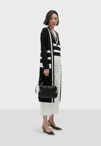 Svart- och vitrandig lång cardigan över en randig topp, ihop med ljusa byxor. Svart kviltad handväska med kedjeaxelrem och klackskor.