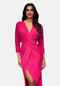 Vaaleanpunainen kietoutuva mekko, joka on tehty sileästä kankaasta ja jossa on syvä V-pääntie sekä kolme neljännesosaa pitkät hihat. Suunnittelussa on sivureikä ja diagonaaliset laskokset.