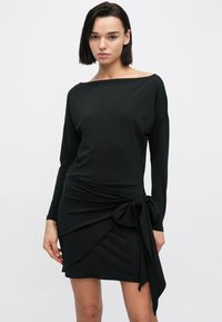 Czarna sukienka z długim rękawem i odkrytymi ramionami, z marszczoną talią i wiązaniem na boku. Wykonana z gładkiego, elastycznego materiału.