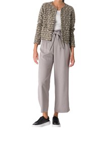 Veste texturée kaki, haut blanc, pantalon large gris avec une ceinture, et baskets noires. Accent sur le contraste des motifs et des couleurs dans les tissus.