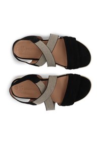 Schwarze Wildledersandalen mit elastischen Kreuzriemen, beigen Akzenten und gepolstertem Fußbett. Flache Sohle sichtbar, mit hellen Kanten.