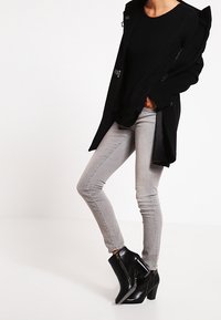 Svart ytterrock med silverdetaljer, stickad svart tröja, ljusgrå skinny jeans och svarta klackiga ankelskor med sidodragkedjor.