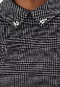 Grå hundtandspatentkappa med en klassisk krage och dekorativa klara ädelstenar vid kragepunkterna.