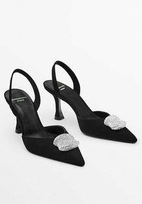Svarta mocka slingback-klackar med spetsiga tår, prydda med en silverfärgad strassspänne och en kort, tjock klack.