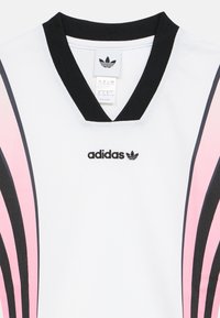 Fehér sportpóló fekete és rózsaszín átlós csíkokkal, fekete V-nyakú gallérral, valamint az elülső részen hímzett fekete Adidas logóval.