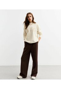 Cremefärgad sweatshirt med "NYC" i fet stil, kombinerad med lösa, högmidjade bruna byxor och vita sneakers. Släta tyger, avslappnad passform.