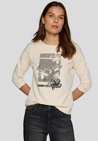 Cremefarbendes Langarmshirt mit floralem Grafikdesign, Text "happy" und schwarzen Akzenten. Kombinieren Sie es mit dunklen Jeans für einen lässigen Look.