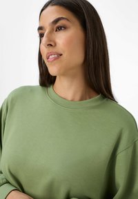 Felpa verde chiaro con scollo rotondo, texture morbida e vestibilità comoda. Maniche lunghe con dettagli di cucitura minimi.
