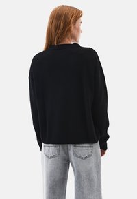 Mustat neulotut neuleet löysällä leikkauksella, pudotetuilla olkasaumoilla ja ribbailla varustetut hihansuut, yhdistettynä vaaleanharmaisiin korkeavyötäröisiin farkkuihin.