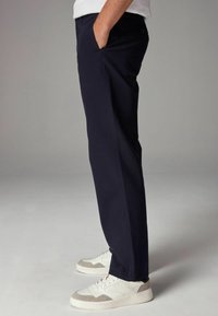 Pantalons en coton bleu marine avec une coupe droite, poches latérales et une texture lisse, associés à des baskets blanches et grises.