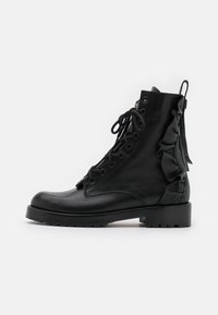 Bottes basses en cuir noir avec bout arrondi, boutonnage à lacets et détails volantés sur le côté. Comprend un talon épais et une semelle texturée.