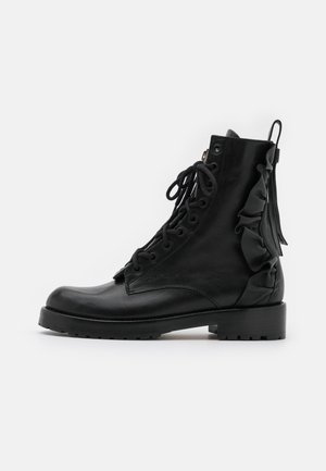 Botines de cuero negro con puntera redonda, cierre frontal con cordones y detalle fruncido en el lateral. Presentan un tacón grueso y suela texturizada.