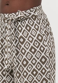 Pantalons à larges jambes marron et blanc avec une taille à nouer. Présente un imprimé géométrique en losanges et un tissu texturé.