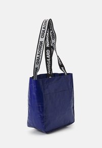 Sac fourre-tout bleu en matériau brillant, doté de bretelles à logo imprimé noir et blanc, de forme carr�ée et d'une poche avant.